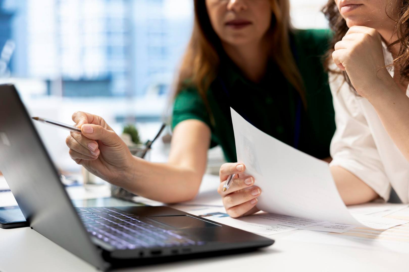 Zwei Personen arbeiten gemeinsam am Laptop und prüfen Dokumente im Büro